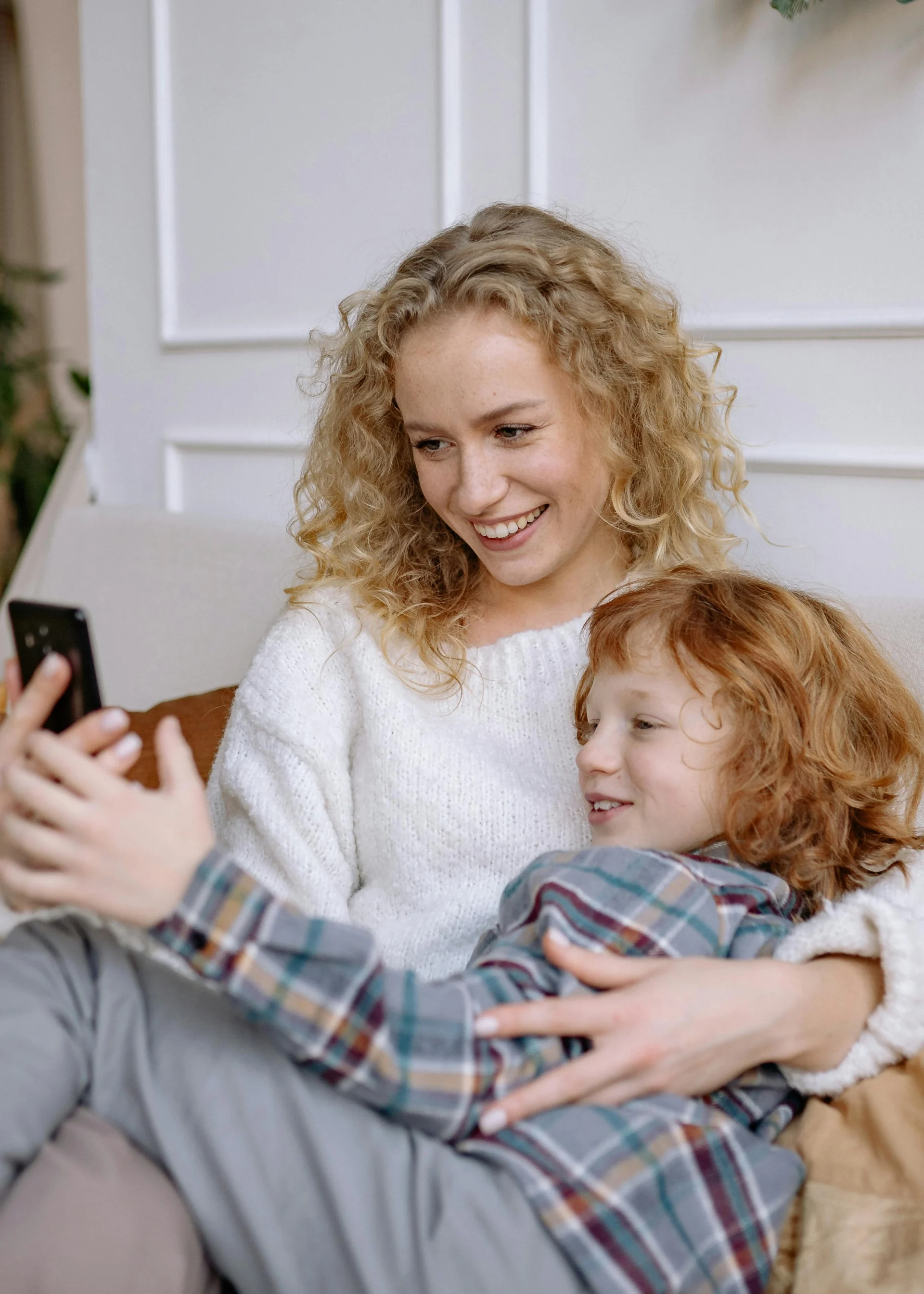 A joyful mother and her son smiling as they take a selfie indoors, capturing a heartfelt family moment.